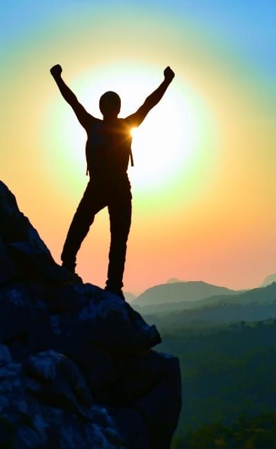 Man on cliff with arms raised in victory